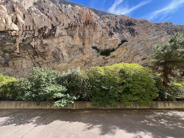 La falaise de Samatan : une paroi de calcaire clair strié d'ocre, au-dessus de la végétation et de la route devant l'immeuble.