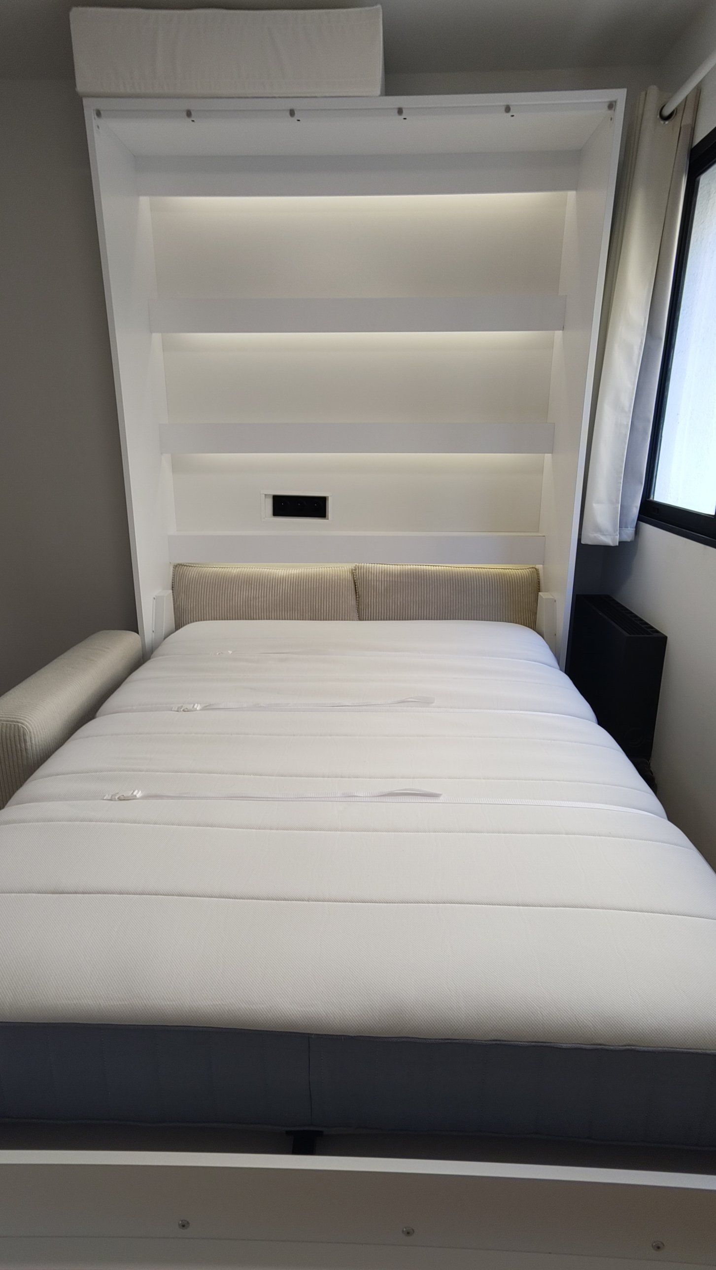Gros plan sur le lit déplié : matelas, coussins en velours côtelé, étagères éclairées en LED et prises.